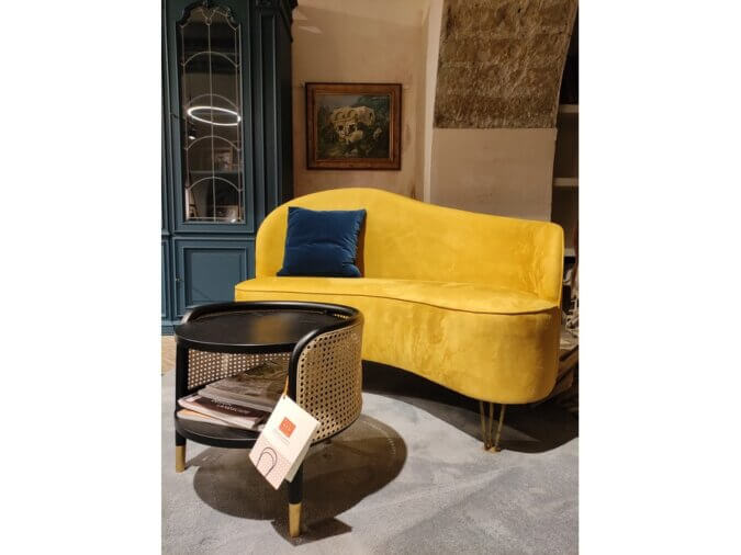 Curved Sofa giallo con un cuscino blu su un tappeto blu cielo. Tavolino davanti ed una madia blu dietro.